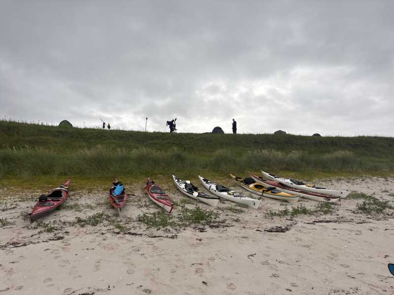 Eight sea kayaks lined up on the sand below the camp at Isle Ristol